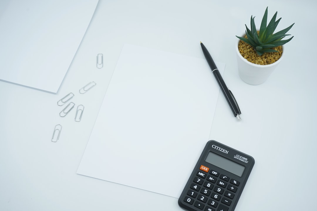 A desk scene with blank papers, a calculator, a pen, paper clips, and a small plant.